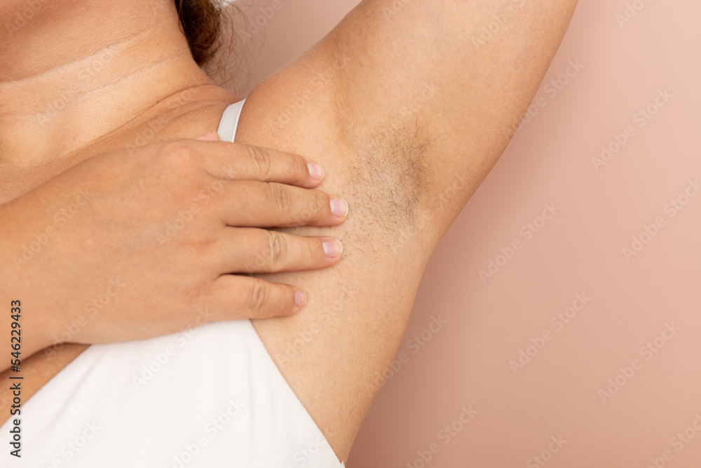 Woman touch hairy underarms with hand closeup, free copy space, beige background. Raised arm with armpit hair. Female beauty trend, freedom, feminism, body positive, naturalness. Hygiene concept. Woman touch hairy underarms with hand closeup, free copy space, beige background. Raised arm with armpit hair. Female beauty trend, freedom, feminism, body positive, naturalness. Hygiene concept.