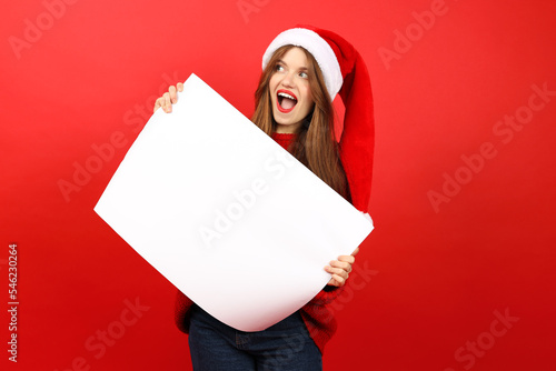 A young woman is holding a white poster for advertising or text on a red background. Christmas sale and discounts.