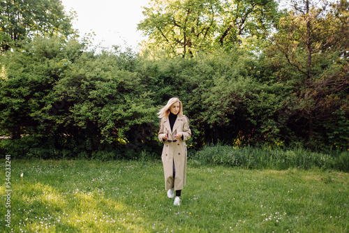 Caucasian blonde woman wearind trench smile happily on sunny spring day outside walking in park photo