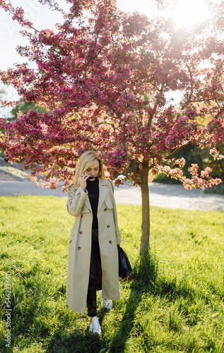 Caucasian blonde woman wearind trench smile happily on sunny spring day outside walking in park photo