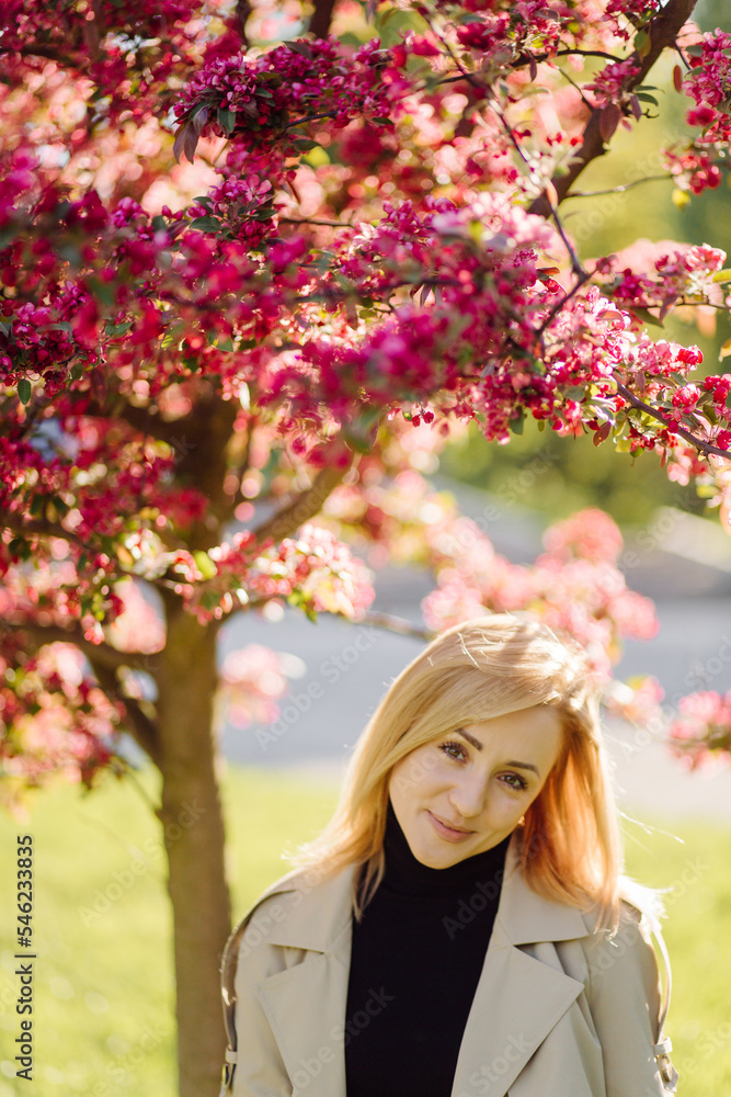 Caucasian blonde woman wearind trench smile happily on sunny spring day outside walking in park Caucasian blonde woman wearind trench smile happily on sunny spring day outside walking in park