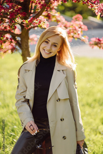 Caucasian blonde woman wearind trench smile happily on sunny spring day outside walking in park photo