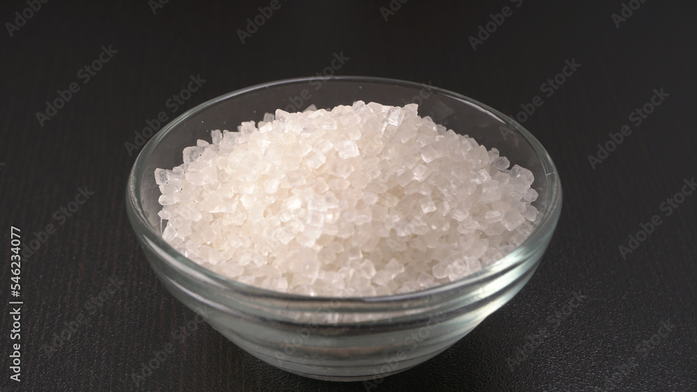 Bowl and spoon with sugar on wooden background.