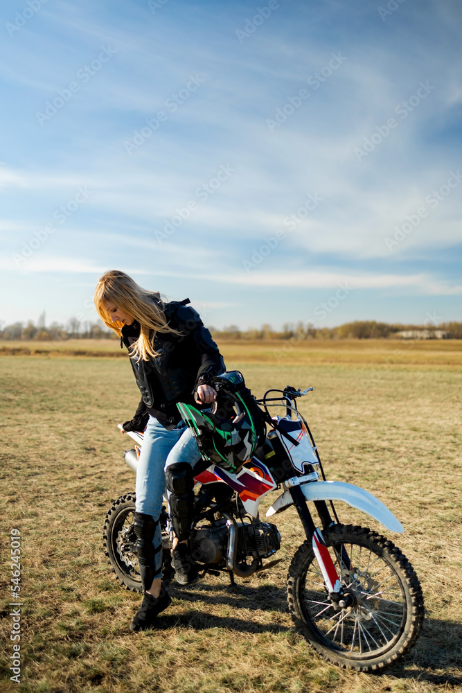 Beautiful blonde woman in motorcycle outfit. Happy female sitting on her motorcycle.