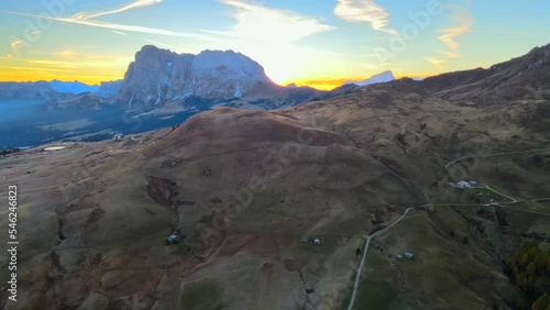 Mountains, forest and grass fields with wooden cabins filmed at Alpe di Siusi in Alps, Italian Dolomites filmed in vibrant colors at sunrise. Filmed with a drone with left to right movement, wide view photo