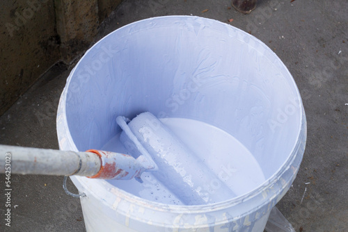 Paint roller in white plastic bucket in construction site.