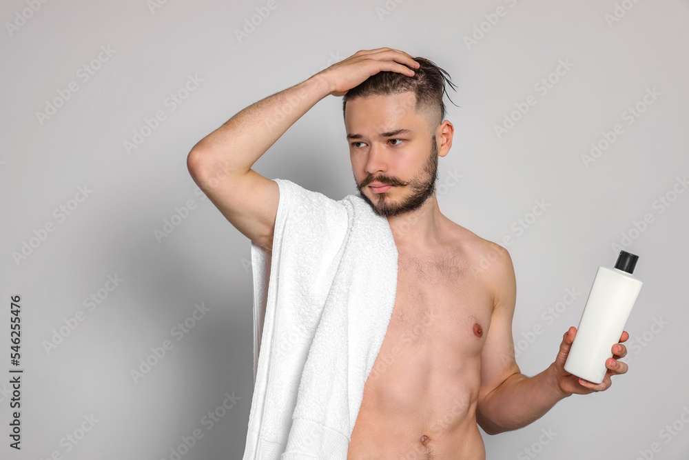Naked man with towel and bottle of shampoo on light grey background Naked man with towel and bottle of shampoo on light grey background