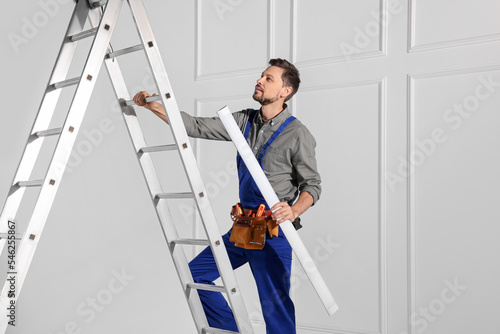 Electrician in uniform with ceiling lamp on metal ladder indoors