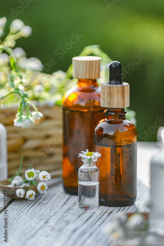 Bottles of chamomile essential oil and flowers on white wooden table  closeup