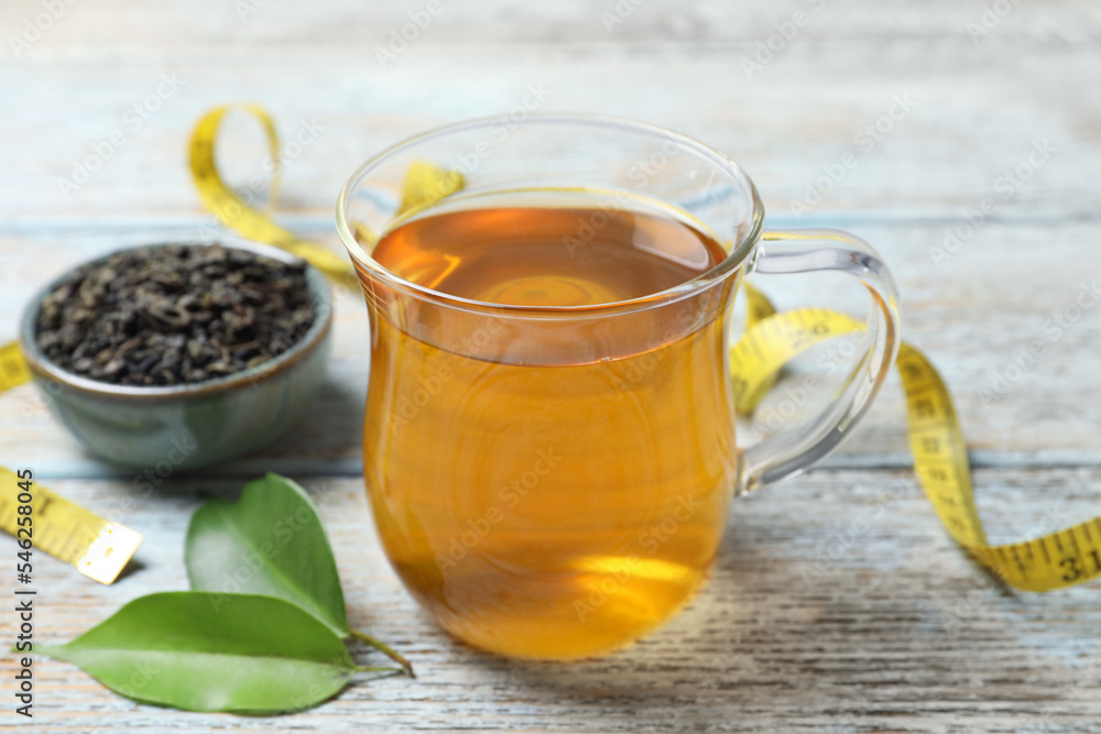 Cup of herbal diet tea, measuring tape and green leaves on wooden table, closeup. Weight loss concept Cup of herbal diet tea, measuring tape and green leaves on wooden table, closeup. Weight loss concept