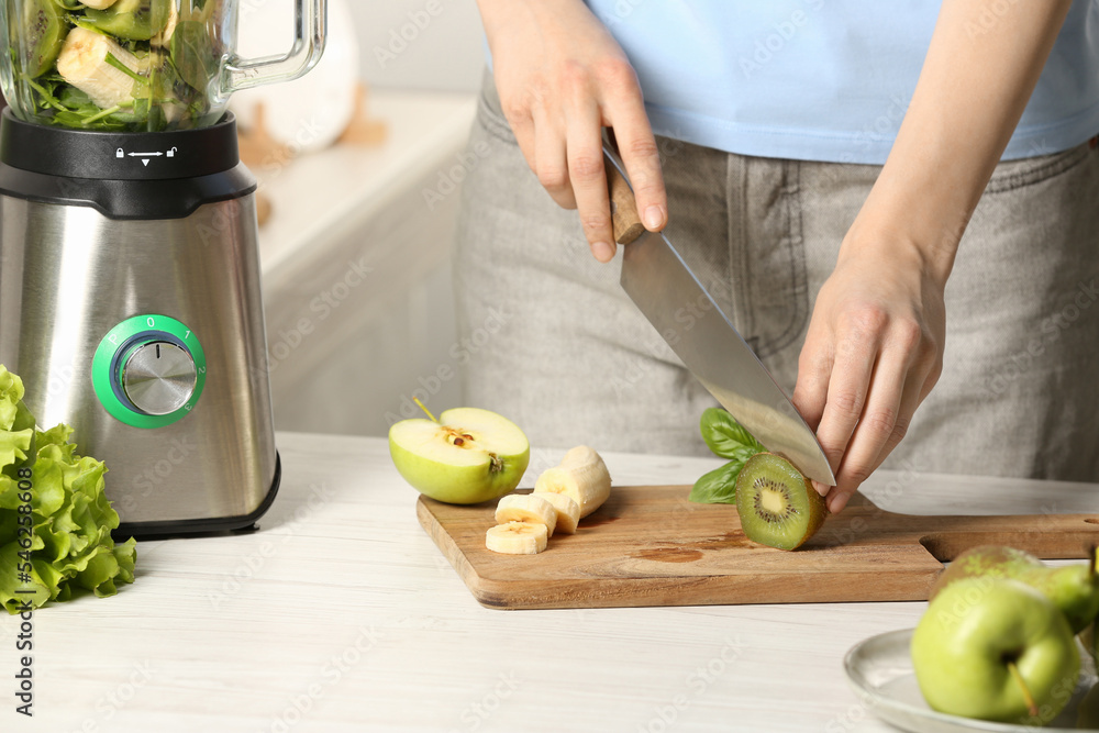Woman preparing ingredients for tasty green smoothie at white wooden table in kitchen, closeup Woman preparing ingredients for tasty green smoothie at white wooden table in kitchen, closeup