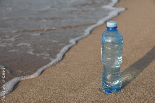 Plastic bottle of fresh water on wet sand near sea. Space for text