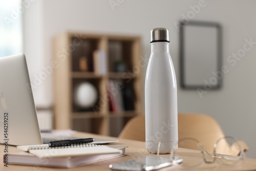 White thermos bottle on wooden table indoors. Space for text