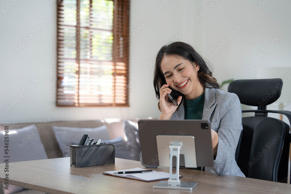 Smiling beautiful Asian businesswoman analyzing chart and graph showing changes on the market and holding smartphone at office. Smiling beautiful Asian businesswoman analyzing chart and graph showing changes on the market and holding smartphone at office.