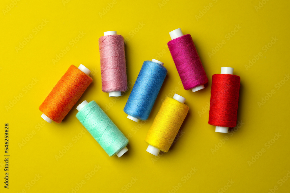 Different colorful sewing threads on yellow background, flat lay Different colorful sewing threads on yellow background, flat lay