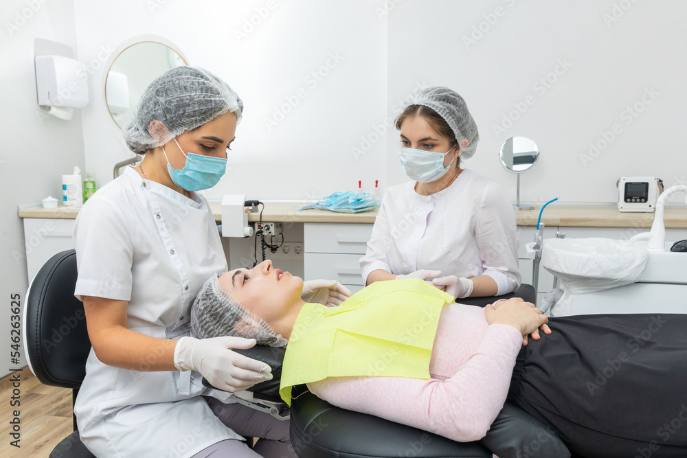 Dentist and assistant performing dental treatment inmodern dental clinic, patient laying in a chair Dentist and assistant performing dental treatment inmodern dental clinic, patient laying in a chair