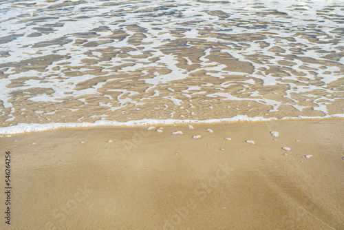 Close-up of a sandy beach with a transparent wave. Sea coast on a summer day.
