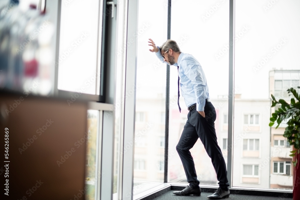 Full length of worried businessman standing at the office by the window Full length of worried businessman standing at the office by the window