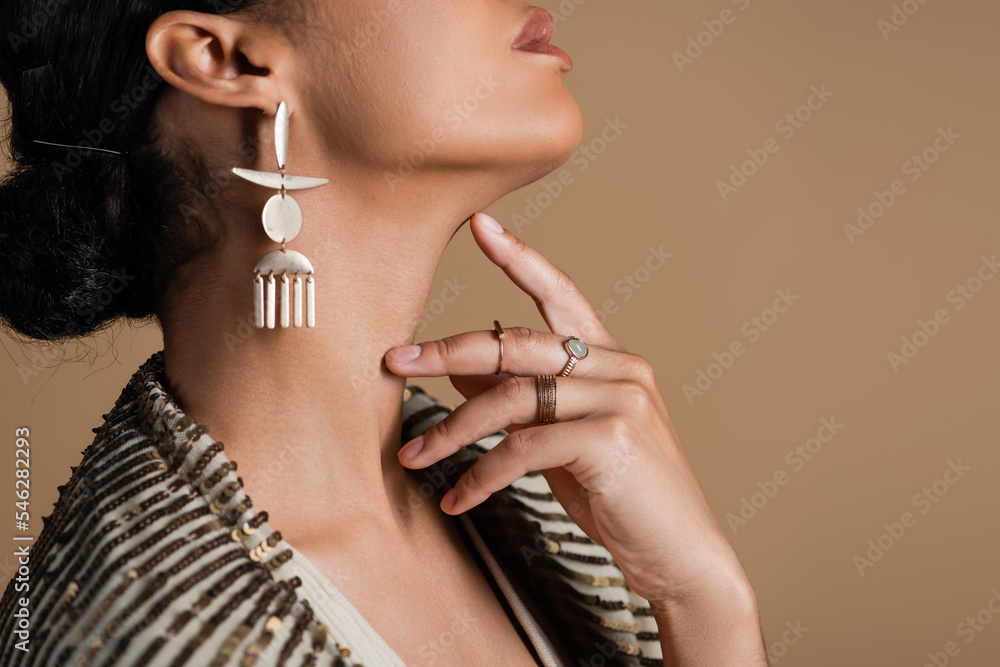 cropped view of young african american woman in luxurious golden jewelry posing isolated on beige.