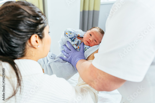Unrecognizable doctor giving newborn baby boy hispanic woman after birth in postnatal hospital. © Iryna