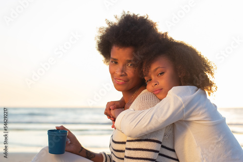 Portrait of satisfied family at sunset. Mother and daughter smiling, hugging, looking at camera. Family, love, bonding concept