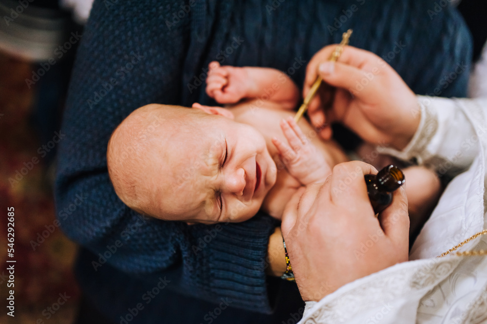 The priest in the church conducts a sacred rite, the ritual of anointing the head of a newborn crying child. Close-up photography, religion.