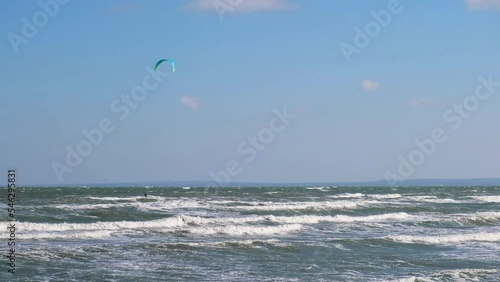 A man in a wetsuit on a parachute rides a board on the waves of the sea. A young man performs a trick in the air against the sky. Water sports, kitesurfing, paragliding, hydrofoil, surfing photo