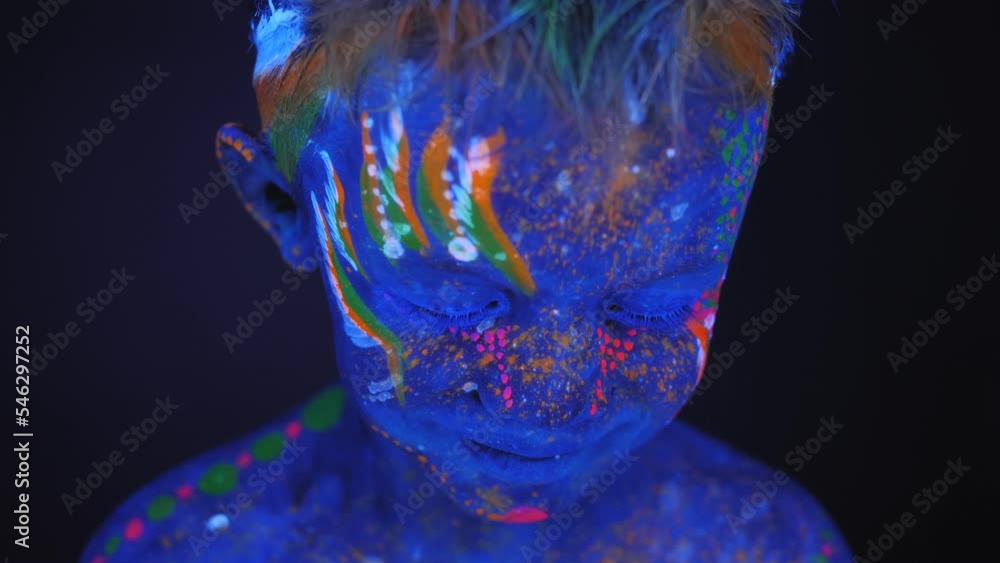 Close-up of a little boy's face with an ultraviolet pattern on his body, he smiles. Under fluorescent lighting, the eyes appear black. Close-up of a little boy's face with an ultraviolet pattern on his body, he smiles. Under fluorescent lighting, the eyes appear black.