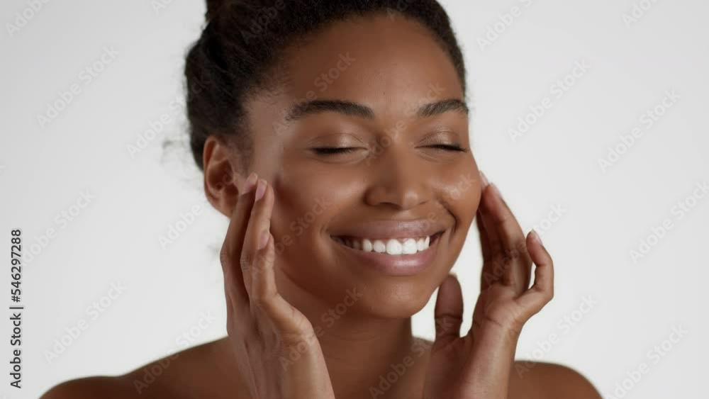 Face yoga concept. Young happy african american woman massaging her face and smiling aside, white background Face yoga concept. Young happy african american woman massaging her face and smiling aside, white background
