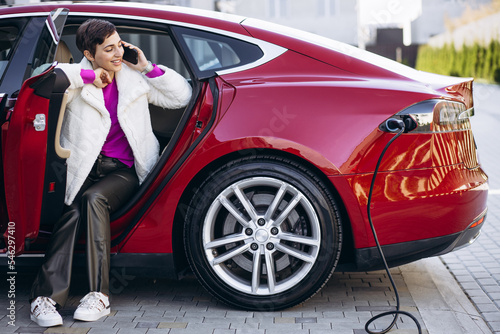 Woman charging electric car and talking on the phone © Petro