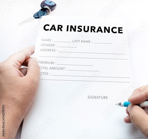 Closeup of hands signing car insurance document. Buying or selling new or used vehicle with car keys on table concept