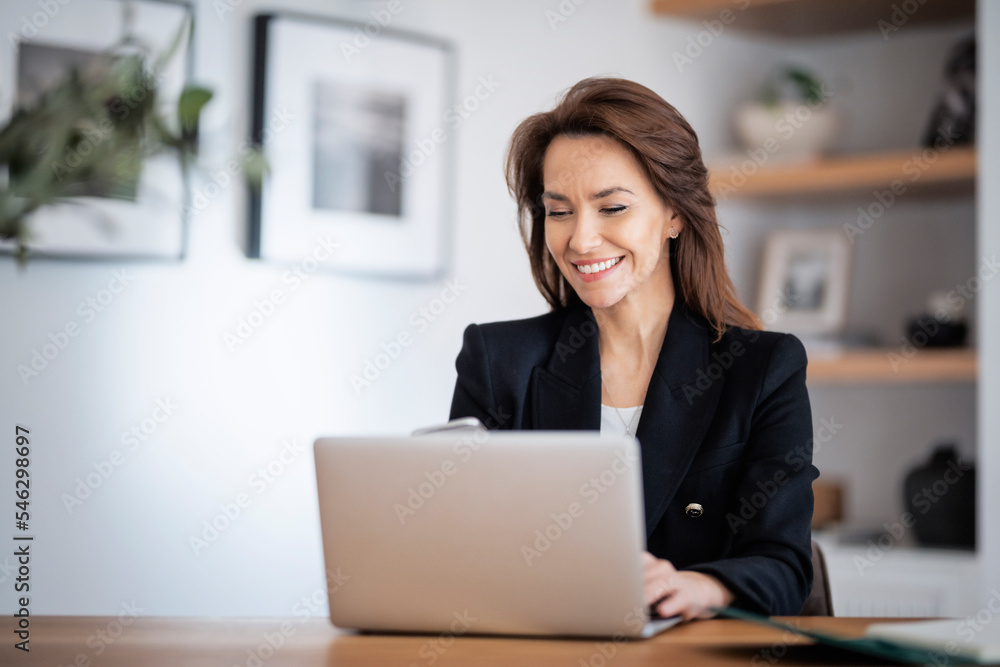 Happy woman sitting at table and using laptop while working from home Happy woman sitting at table and using laptop while working from home
