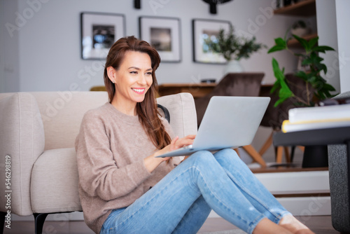 Smiling caucasian woman using laptop at home while sitting on the floor