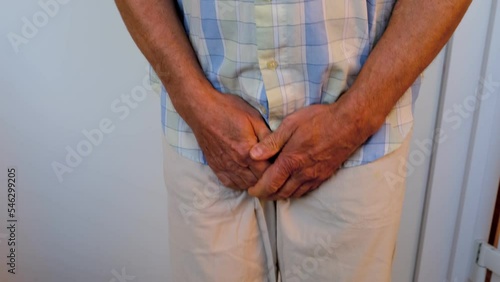 man in beige trousers, male hands on groin, mature man wants to go to toilet, senior 60 years old feels discomfort, concept of men's health, age-related urinary incontinence photo