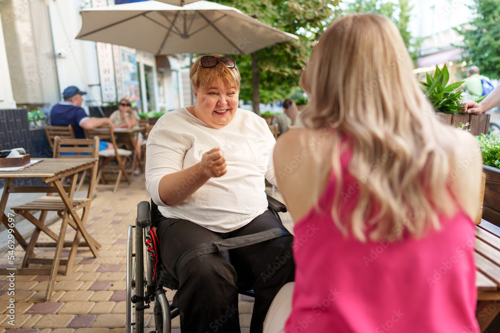 Mother with disability in wheelchair talking to her daughter while sitting at the table in cafe Mother with disability in wheelchair talking to her daughter while sitting at the table in cafe