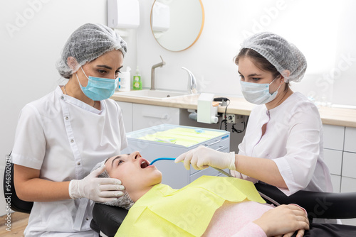 Professional dentist surgeon and assistant performing dental operation in a clinic with modern equipment