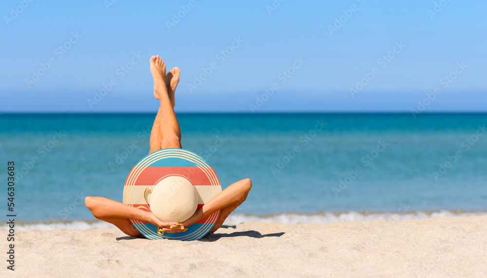 Fototapeta premium A girl on the beach in a straw hat in the colors of the transgender flag. Focus on the hat.
