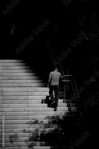 Vertical shot of a man climbing up the stairs in grayscale