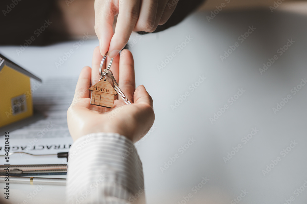 Obraz premium A home rental company employee is handing the house keys to a customer who has agreed to sign a rental contract, explaining the details and terms of the rental. Home and real estate rental ideas.