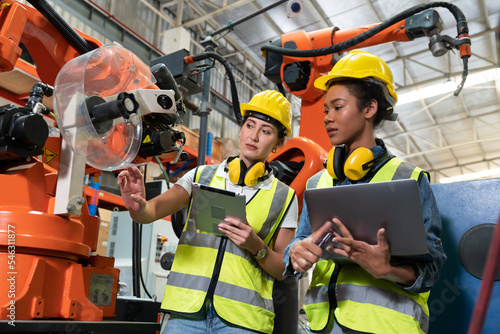 Fotografija Female automation engineers in safety vest with yellow helmet using laptop for i