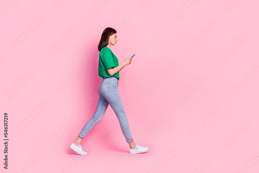 Full length photo of nice young girl walking hold device chatting read news dressed trendy green clothes isolated on pink color background Full length photo of nice young girl walking hold device chatting read news dressed trendy green clothes isolated on pink color background