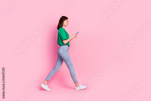 Full length photo of nice young girl walking hold device chatting read news dressed trendy green clothes isolated on pink color background