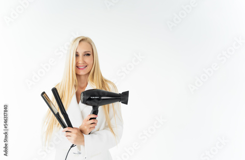 Stylish european woman hairdresser smiling and holding black hair dryer and curling iron in her hands.Isolated on white background, Hair care concept