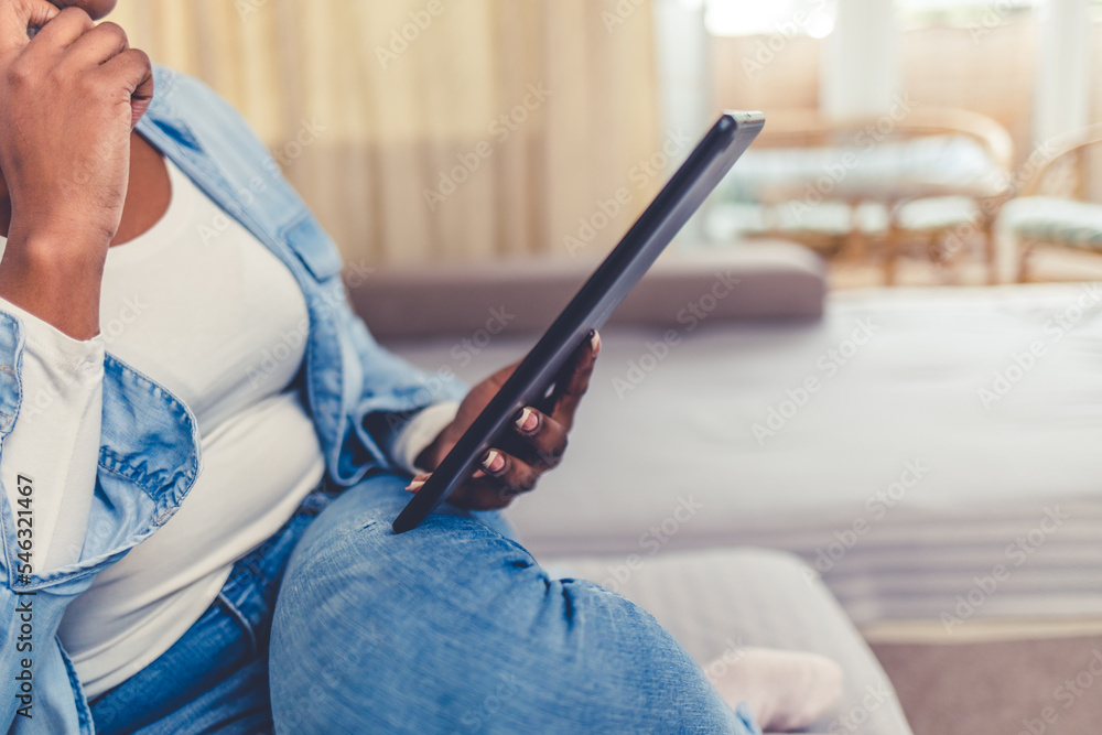 Fototapeta premium Cropped shot of a beautiful young woman using a digital tablet while relaxing on her sofa at home
