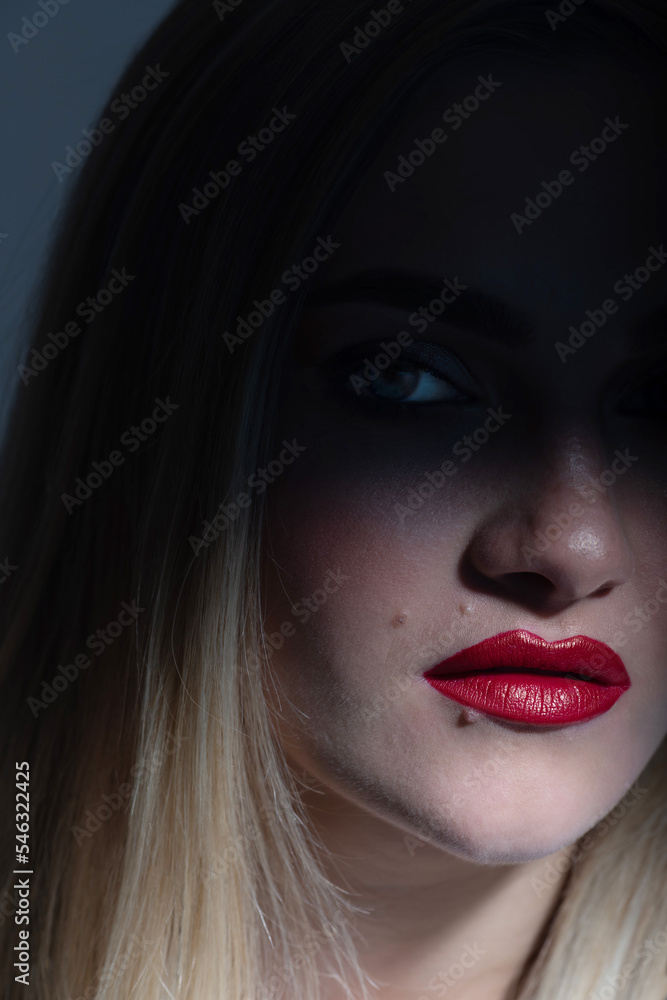 Fashion and make-up concept. Beautiful blonde woman portrait partly face covered with shadow. Mouth and nose illuminated with light. Model looking at camera. Red lipstick make-up Fashion and make-up concept. Beautiful blonde woman portrait partly face covered with shadow. Mouth and nose illuminated with light. Model looking at camera. Red lipstick make-up
