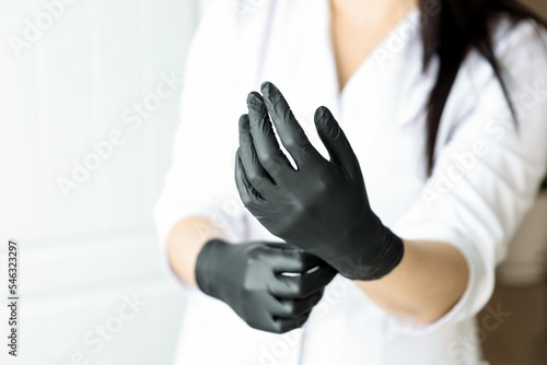 Cosmetologist or doctor woman hands in black latex gloves on white background prepairing for a procedure or operation