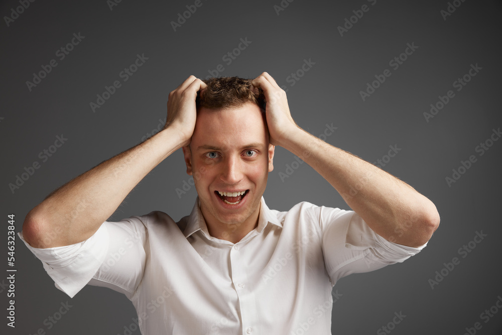 Portrait of young man emotionally posing in white shirt isolate over grey studio background. Shocked, surprise Portrait of young man emotionally posing in white shirt isolate over grey studio background. Shocked, surprise