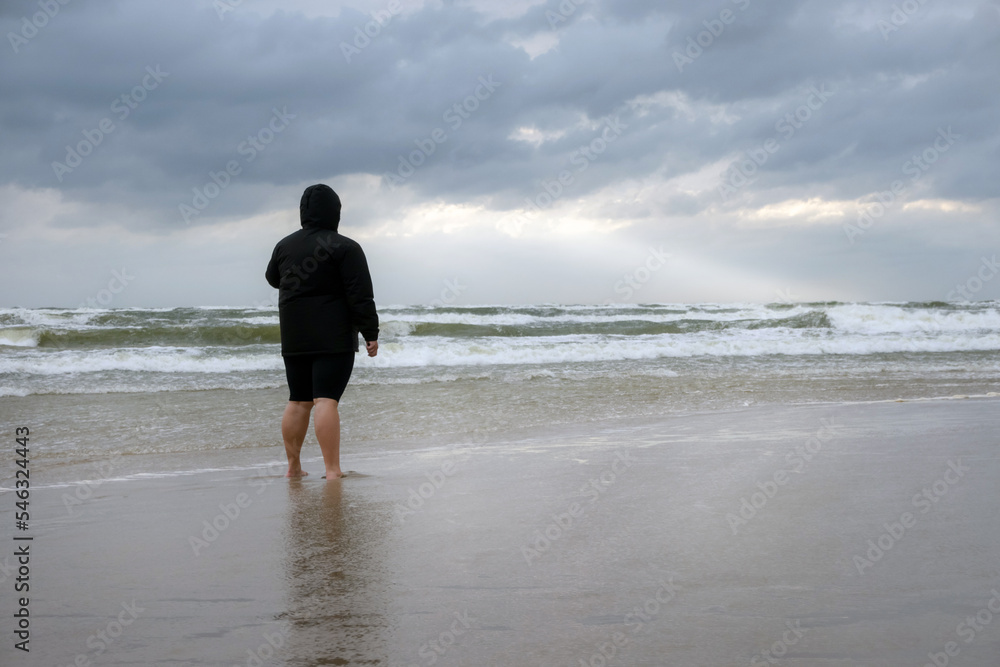 Person standing on the beach on the cloudy day. Sea shore after the storm with the woman looking at the horizon. Person standing on the beach on the cloudy day. Sea shore after the storm with the woman looking at the horizon.