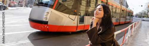Photography Trendy young woman in coat standing near road with tram on street in Prague, banner