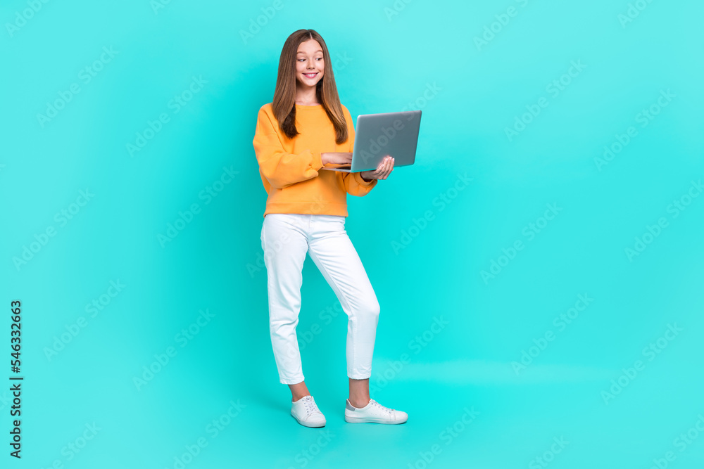 Full length size photo of positive cute teenager girl wear stylish outfit hold computer online chatting with teacher isolated on cyan color background Full length size photo of positive cute teenager girl wear stylish outfit hold computer online chatting with teacher isolated on cyan color background